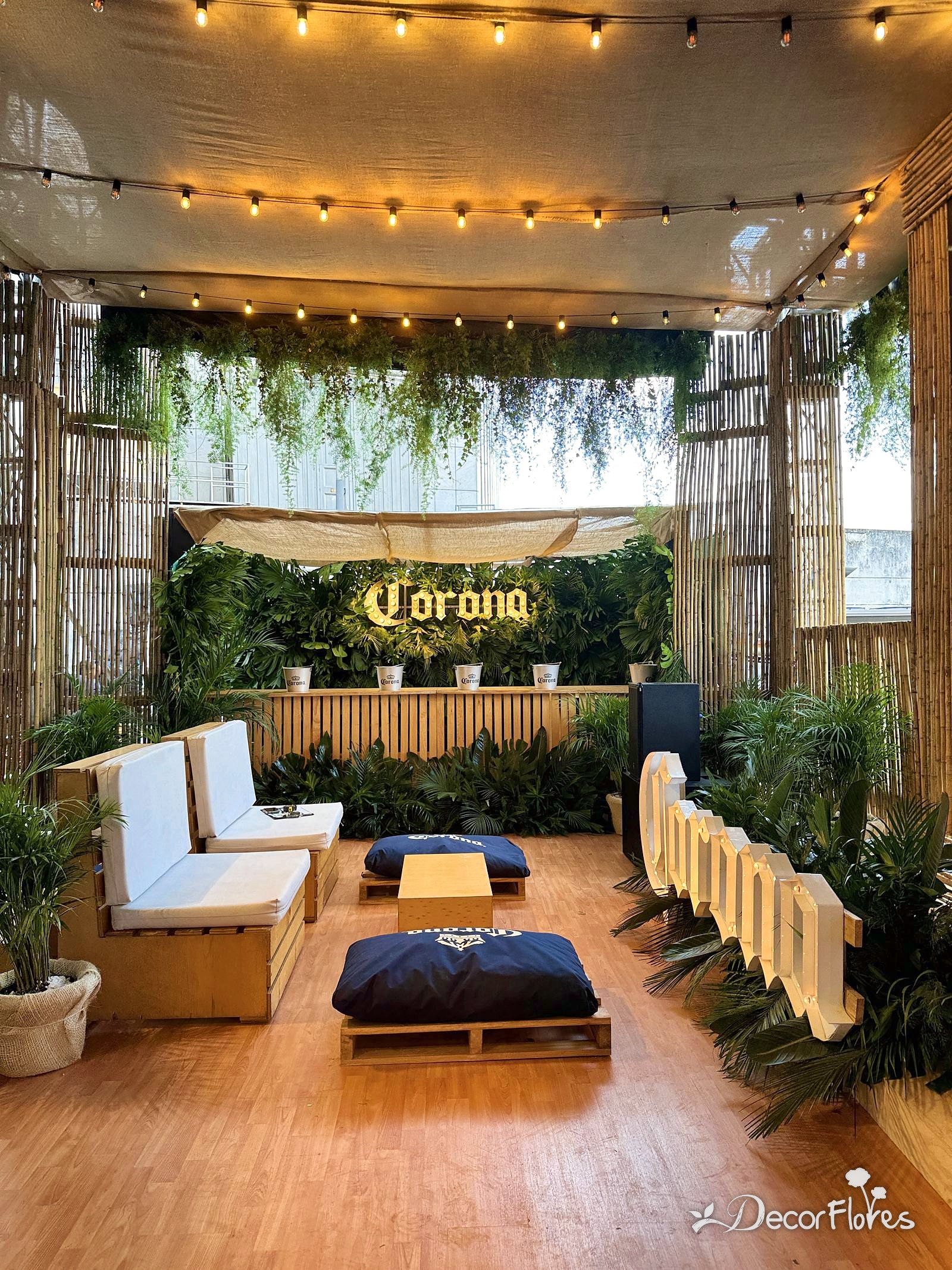 Lounge para una marca de cerveza con techo de follajes, muro verde y letrero iluminado